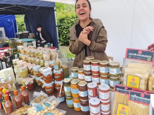 Market stall with savoury products in jars sold by friendly laughing lady