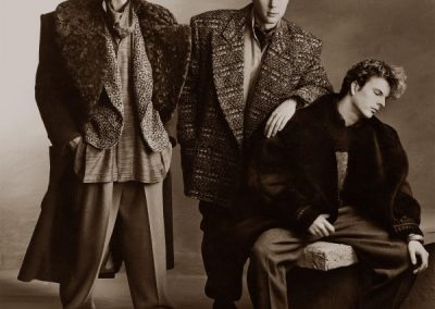 Black & white photo of 3 men posing in a studio in 80s style clothes
