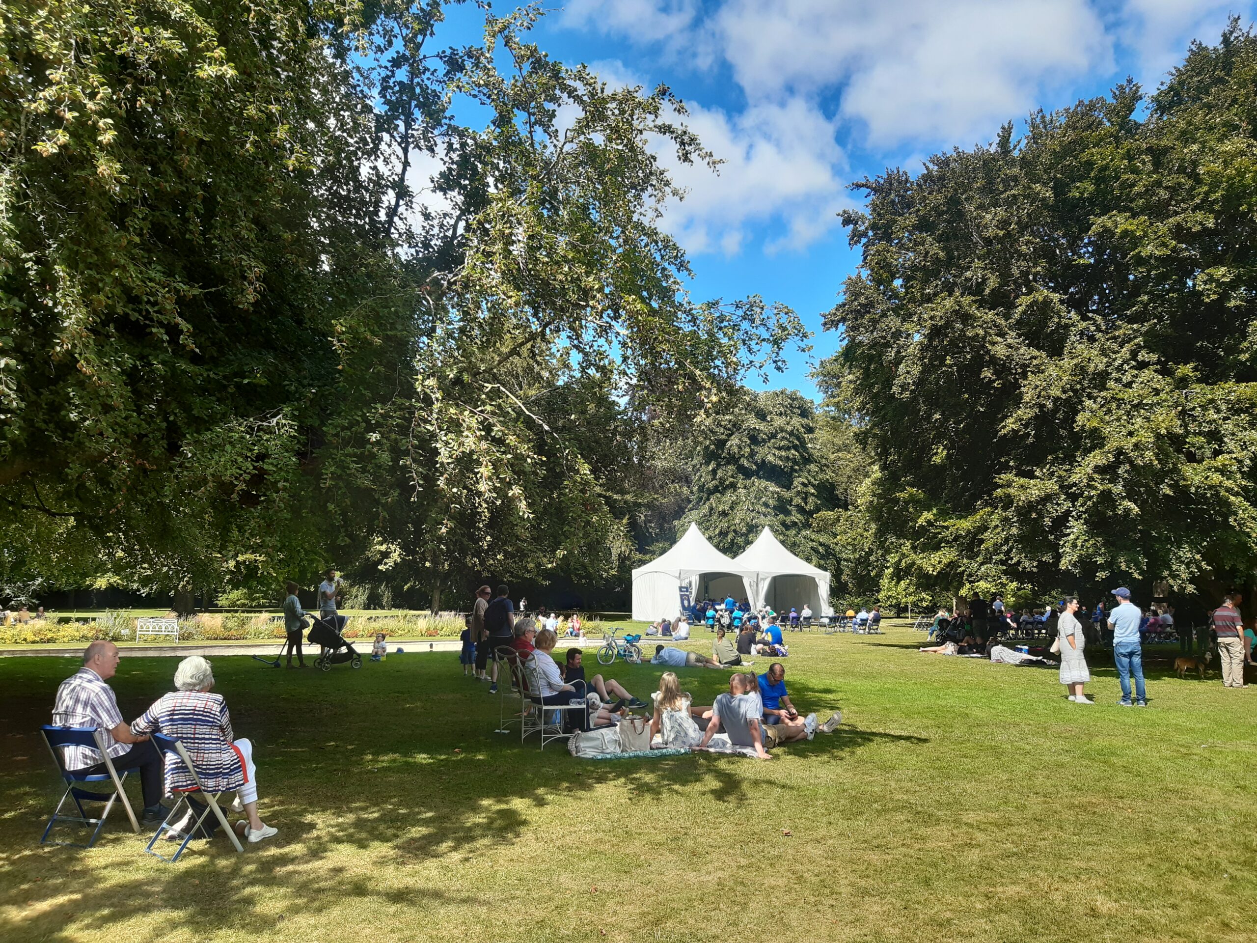 Visitors on the fountain lawn listening to music from brass band in white tent