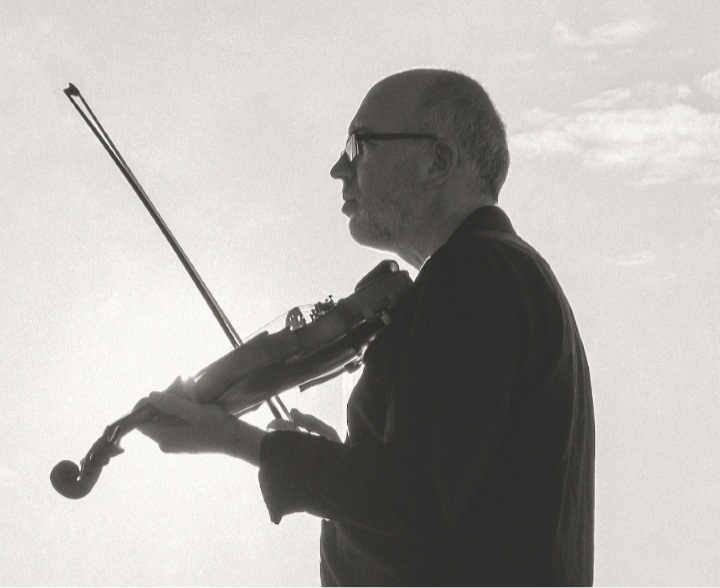 Black & white photo of Toner Quinn holding violin with they sky in the background
