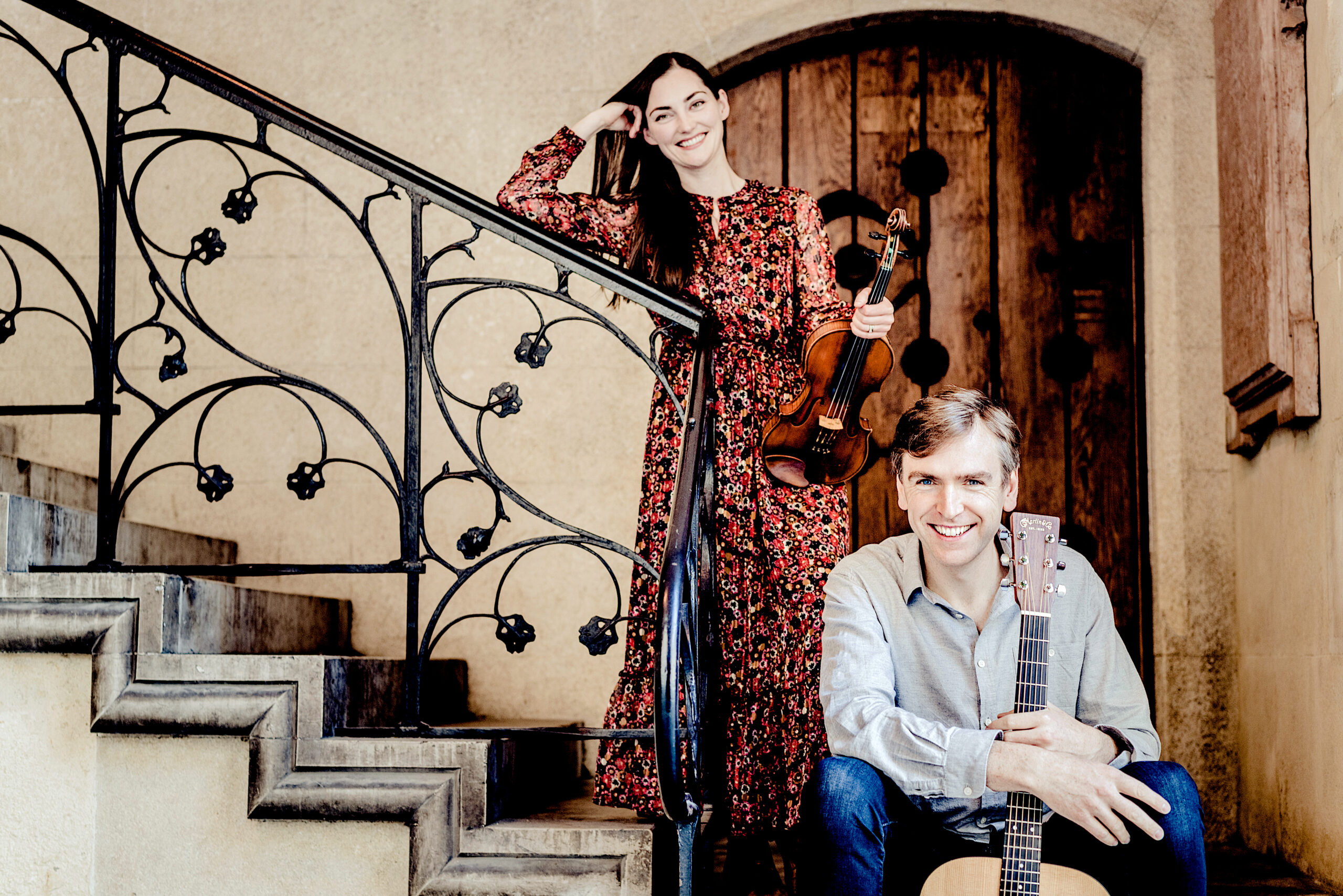 Photo of Zoë Conway holding fiddle & John Mc Intyre holding a guitar on a staircase